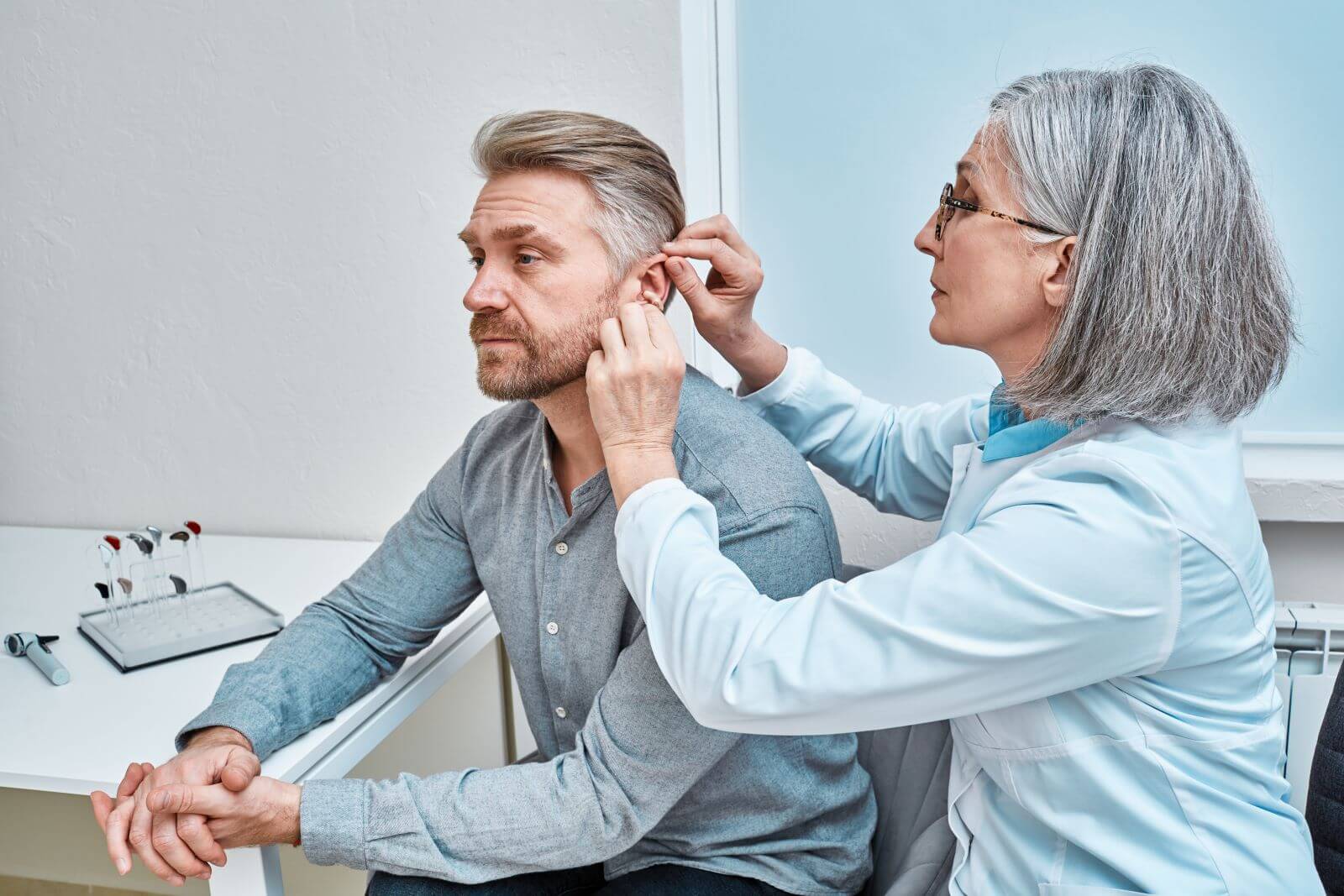 Audiologist fitting a hearing aid to a patient's ear