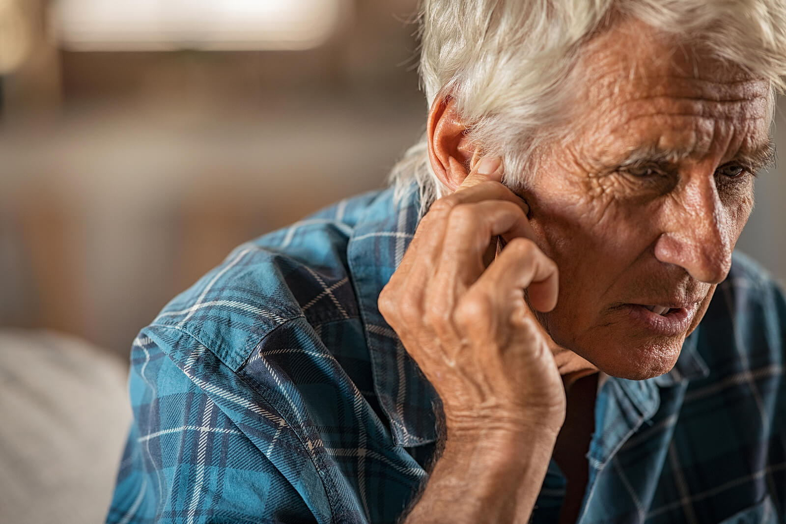 Old man with concerned look on his face holding his ear